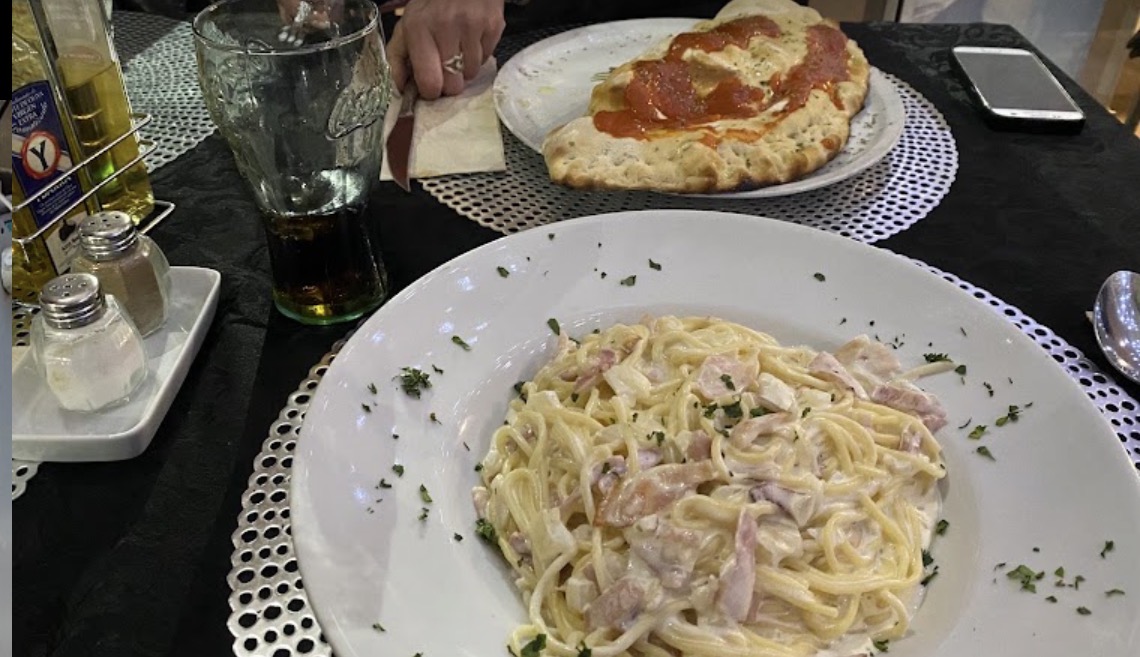 Plato de espaguetis carbonara junto a una pizza abierta